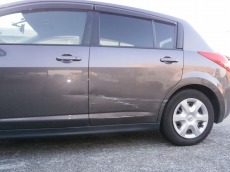 修理前の日産ティーダの左側面。左フロントドアからリヤドア、後輪周辺のクォータパネルにかけて、車体下部に横に長く連続するへこみと擦りキズがある状態。